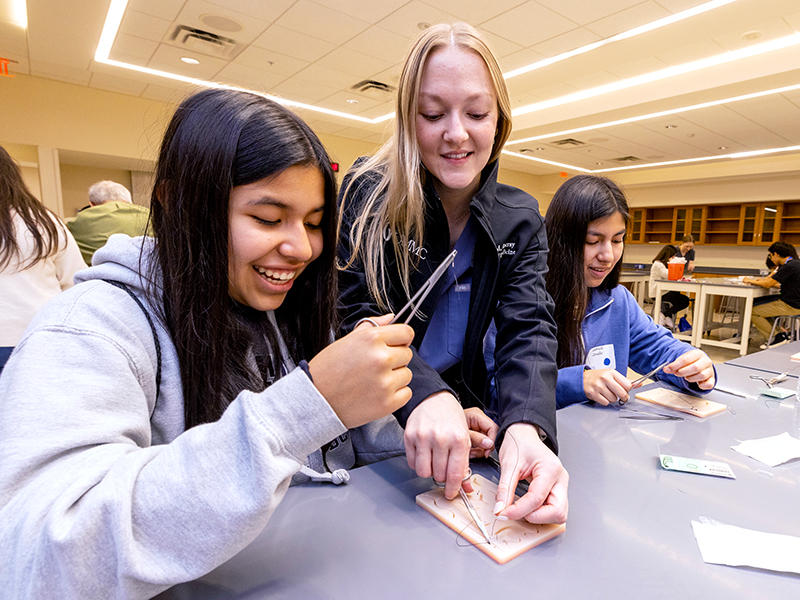 Isabelle Zevallos, left, and her sister, Gabrielle Zevallos, flank medical student Rachel Rocray, who is teaching them the finer points of suturing.